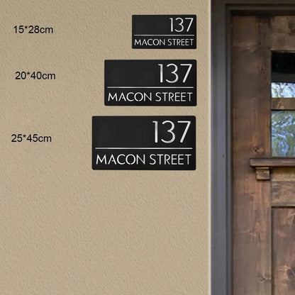 Modern black house number signs '137 Macon Street' in 3 sizes on beige wall near wooden door