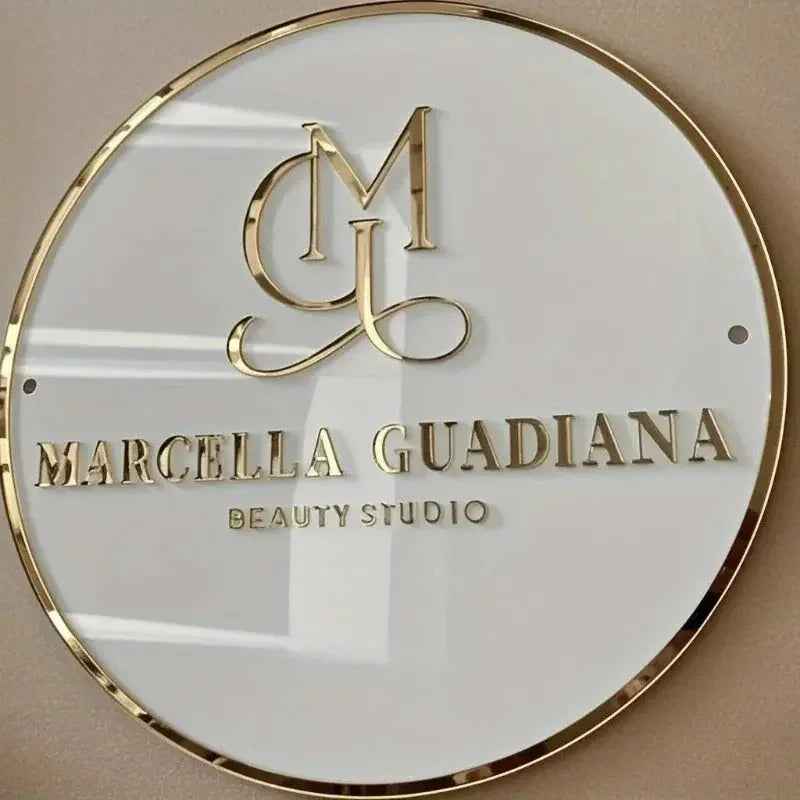 Elegant gold monogram sign for Marcella Guadiana Beauty Studio, round white plaque with metallic lettering
