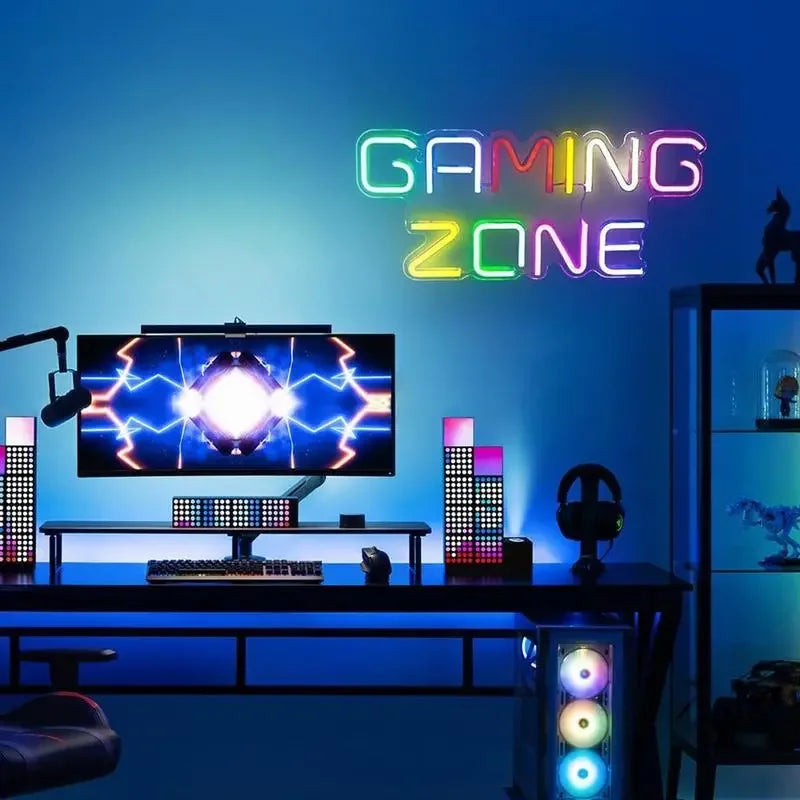 Colorful neon 'GAMING ZONE' sign above gaming desk with RGB lights and monitor