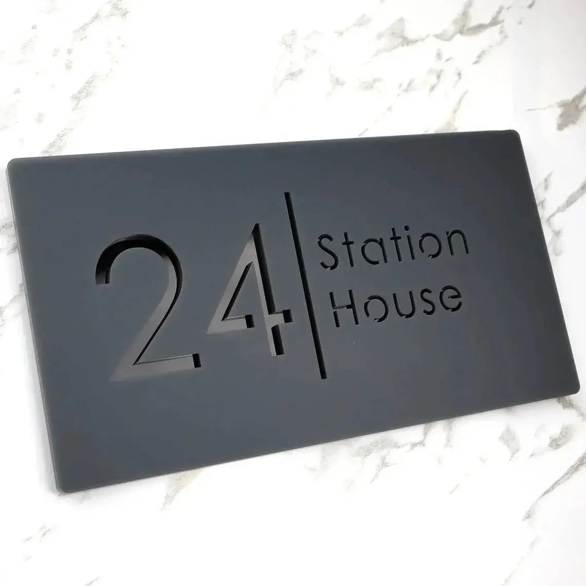 Modern black address plaque with '24 Station House' cutout text on marble surface