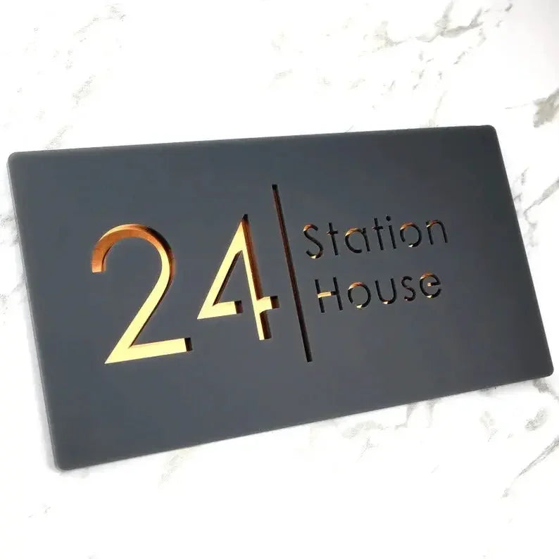 Modern black house sign with gold '24 Station House' lettering on marble surface