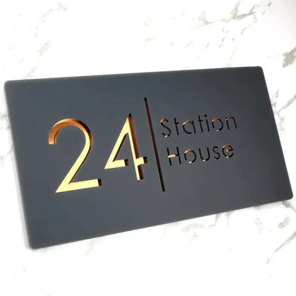 Modern black house sign with gold '24 Station House' lettering on marble surface