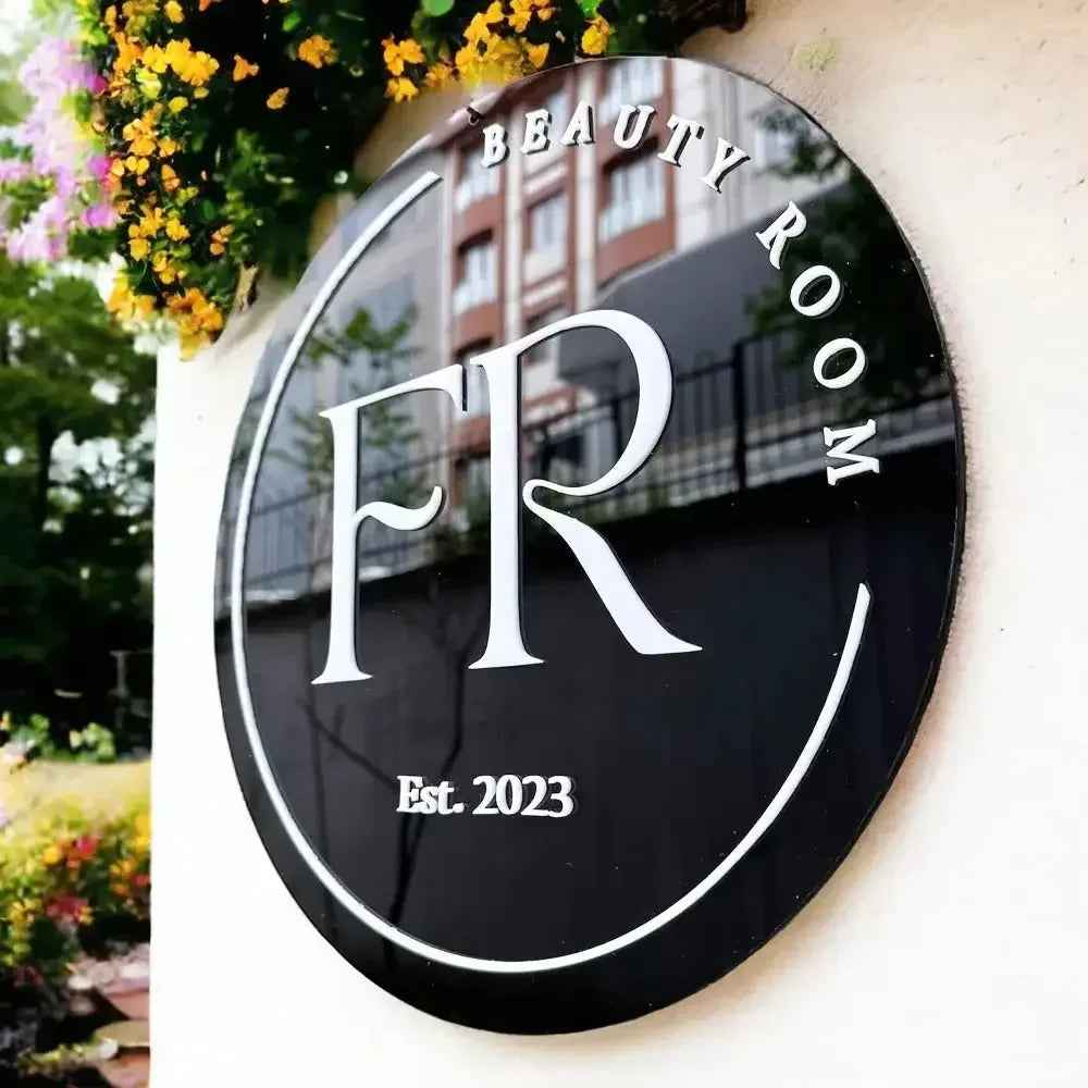 Black oval beauty room sign with FR logo, Est. 2023, mounted on wall with flowers