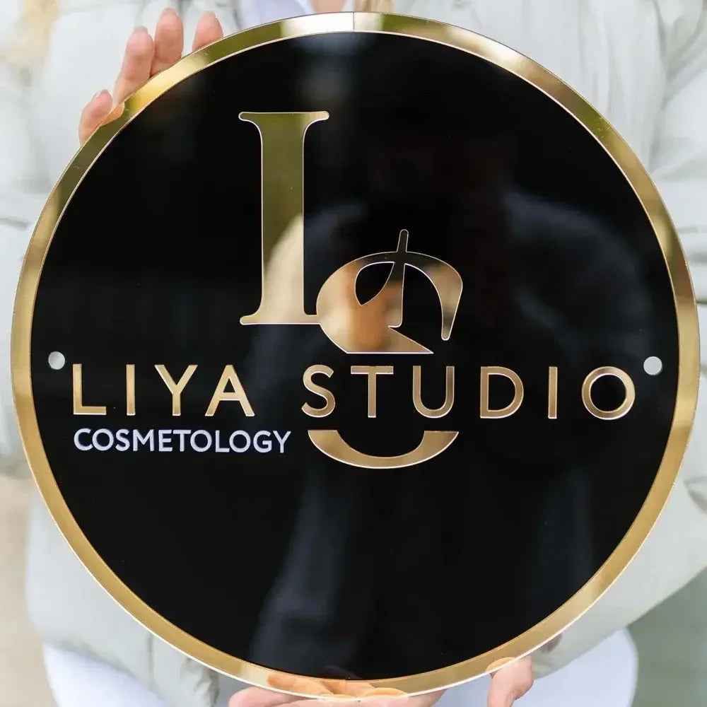 Custom round black and gold sign for Liya Studio Cosmetology, held by hands