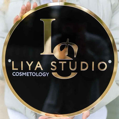 Custom round black and gold sign for Liya Studio Cosmetology, held by hands