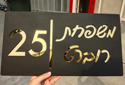 Custom black and gold house number sign with Thai script, held outdoors